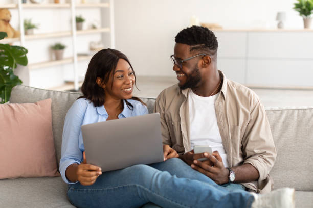 istock Happy black couple sitting on couch, using cellphone and pc 1385175446