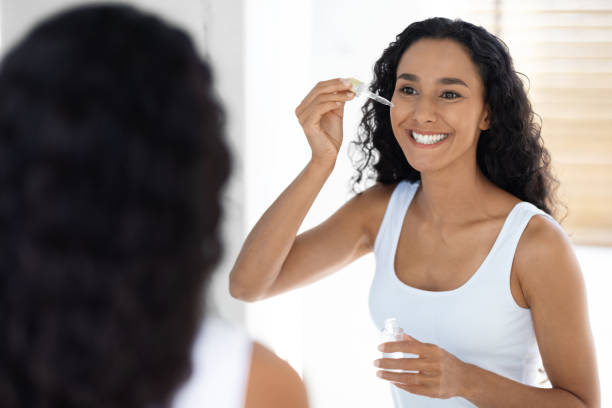 istock Self-Care Routine. Young Beautiful Lady Applying Face Serum With Dropper In Bathroom 1385176700