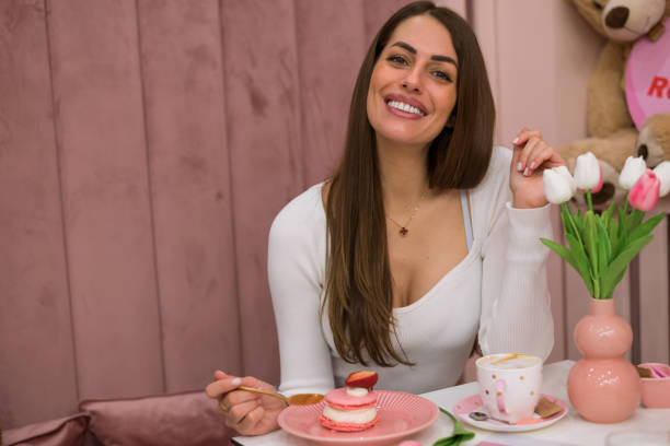 симпатичная улыбающаяся женщина ест вкусные сладкие розовые макаруны, стоковое фото - people cleavage color image clothing стоковые фото и изображения