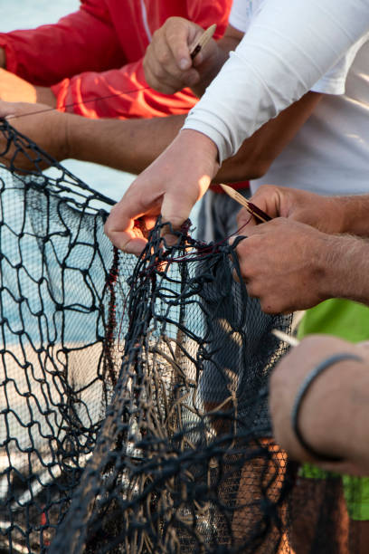 gruppe von fischern, die das fischernetz reparieren - fishermen harbor stock-fotos und bilder