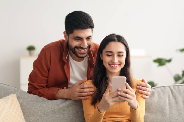 istock Happy Arabic Spouses Using Phone Together Texting Sitting At Home 1385179122