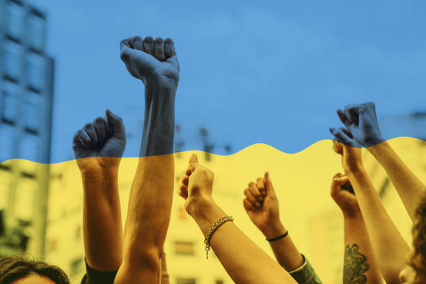 люди с поднятыми кулаками на демонстрации в городе на сине-желтом фоне - protestor protest sign yellow стоковые фото и изображения