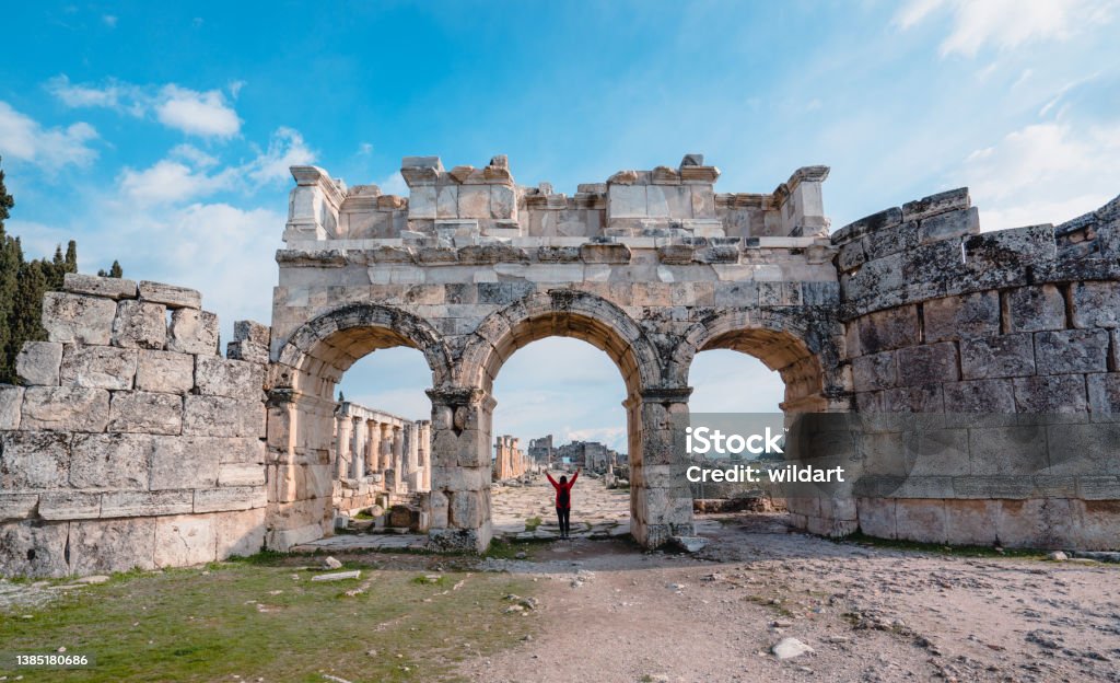 Traveller backpacker girl is open her arms in Frontinus Gate of ancient ruins of Hierapolis , Pamukkale in Denizli UNESCO, arch, Roman Empire, Travertine pools, Greek architecture Hierapolis Stock Photo