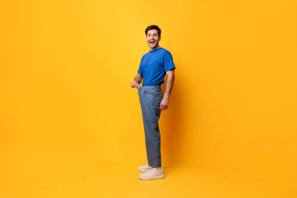 hombre feliz tirando de sus viejos jeans grandes sueltos - loose weight fotografías e imágenes de stock