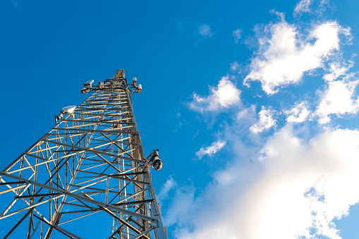 Vertical view of a communications tower showing installed multi-services  telecom equipment including Microwave and 5G cellular repeaters. In view are also installed PTZ CCTV cameras.