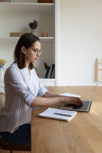 istock Young serious woman sit at table typing on laptop keyboard 1385188685