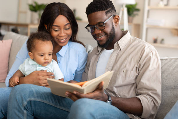 Portrait of happy black family reading book for kid Portrait of millennial black parents reading book to their adorable toddler baby boy at home, sitting on couch in cozy living room, spending time together. Children Development Concept showing photos stock pictures, royalty-free photos & images