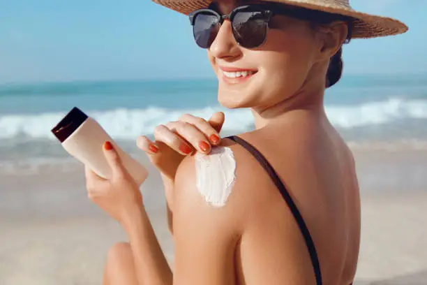 Photo of Girl Using Sunscreen to Skin. Beautiful Woman in Bikini Applying Sun Cream on Tanned  Shoulder. Sun Protection. Skin and Body Care.