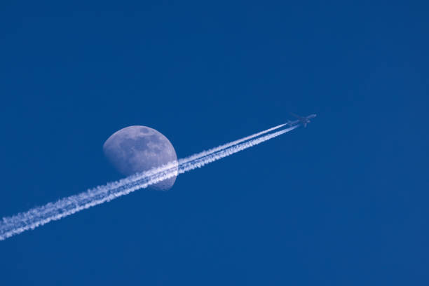 istock Plane flies pass over the moon on blue sky airplane trail 1385195314
