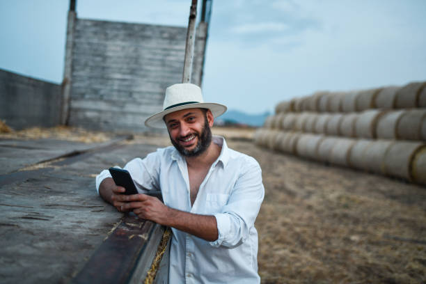 istock Smiling Male Farmer Looking At Social Media On Smartphone While Unloading Haybales 1385195620