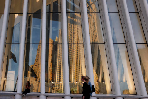 Oculus at World Trade Center in New York New York, United States, 21st September 2017. Reflections in the windows of the Oculus in the World Trade Center, New York, Work of the Spanish architect Santiago Calatrava and inaugurated on March 3, 2016. In the image, two women walk in front of the facade while another young woman looks at her mobile phone. new york life building stock pictures, royalty-free photos & images