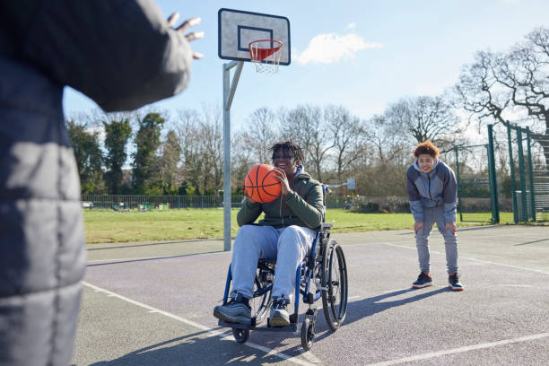 nastoletni chłopiec na wózku inwalidzkim z przyjaciółmi grający razem w koszykówkę w parku - basketball playing ball african descent zdjęcia i obrazy z banku zdjęć