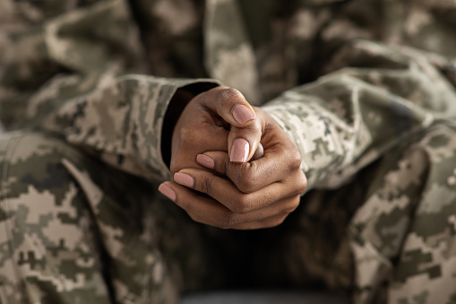 Clasped Hands Of Black Soldier Woman In Camouflage Uniform, Closeup Shot Of Unrecognizable African American Military Lady Sitting On Couch Indoors, Selectife Focus On Fists, Free Space