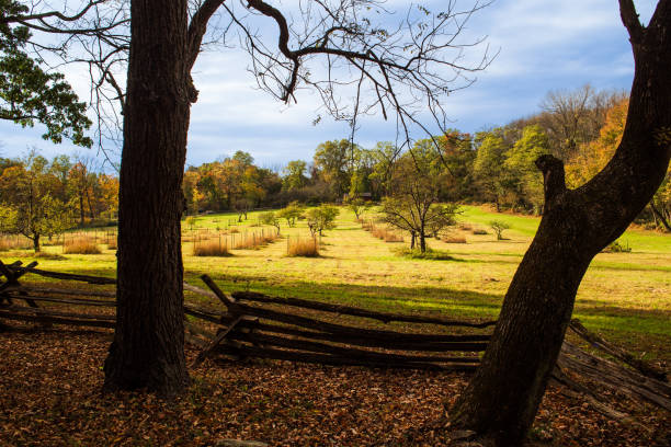 Apple Orchard at Jockey Hollow, Morristown National Historical Park, New Jersey, USA. Fence and tree silhouetted in foreground and the Wick House and forest in distance.  Autumn colors for soft glow.