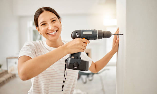 Shot of an attractive young woman standing alone in her home and using a power drill I'm hanging a picture frame up here holding drill stock pictures, royalty-free photos & images