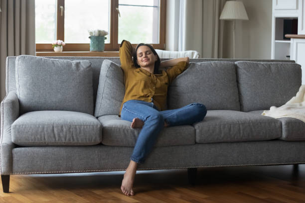 istock Peaceful woman stretching on cozy couch with hands behind head 1385203891