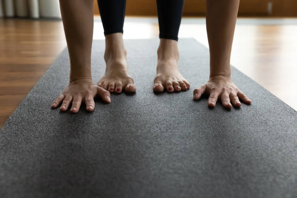 istock Woman standing on mat performs Uttanasana, palms and feet closeup 1385204371