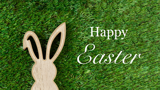 Easter bunny wooden figure against green lawn background and Easter greetings