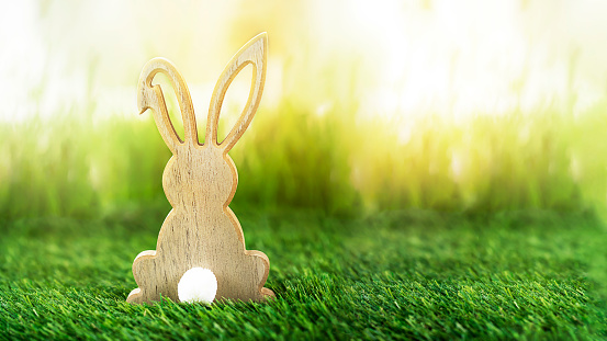 Easter bunny wooden figure on green lawn against bright sunny background