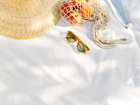 Vintage inspired background with straw hat, female sunglasses and shopper bag with peaches on white towel. Minimalist summer vacation creative still life âfor fashion blog, web, social media, stories.