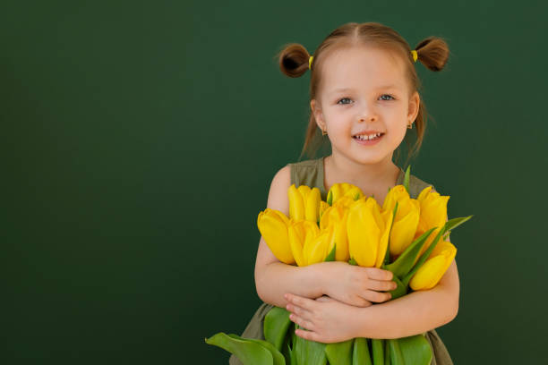 una bambina con le code di cavallo tiene un mazzo di tulipani gialli in braccio per la madre - bouquet tulip flower nature foto e immagini stock