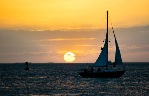 segelschiff bei sonnenuntergang mit sonnenuntergang am horizont. - sailboat sunset nautical vessel sun stock-fotos und bilder