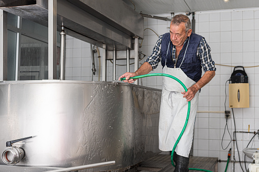 old man in an apron rinse down soap from a stainless steel container. job