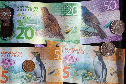 A mixture of New Zealand Bank notes with coins on a black background.