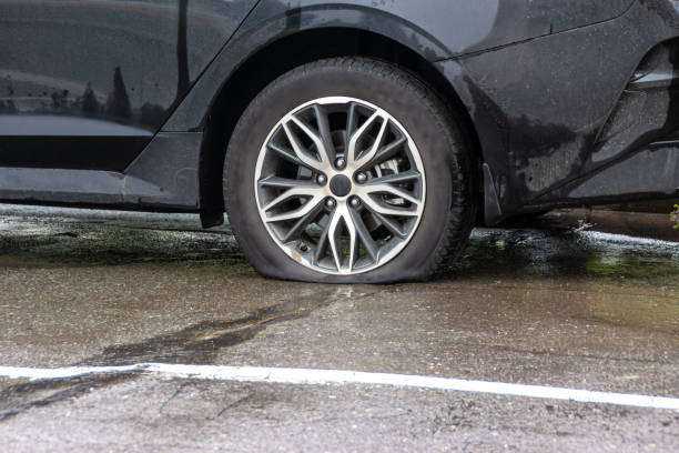 a car with a flat tire stands on asphalt wet from the rain a passenger car with a flat tire stands on the pavement, wet from the rain, waiting for a service car or auto repairman, selective focus flat tire stock pictures, royalty-free photos & images