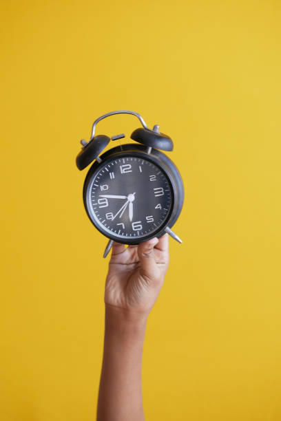 istock person hand holding alarm clock on yellow background , 1385270263