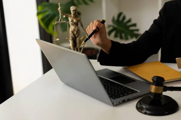 Photo of Attorney in the office with Gail Brass. statue of justice and lawyer working on laptop and the female judge's hammer, or Eustitia. Roman goddess of justice, legal concepts.