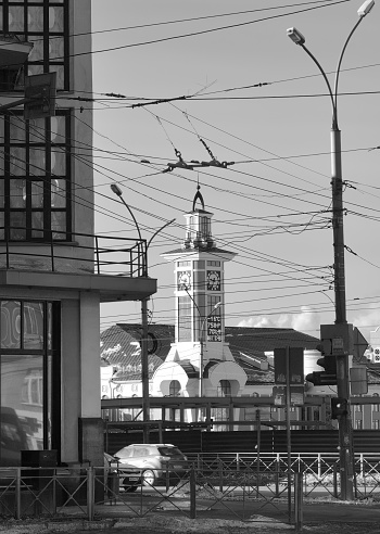 Novosibirsk, Siberia, Russia, 03.12.2022: The tower of the suburban railway station. A stylized clock tower through the thick wires of city streets