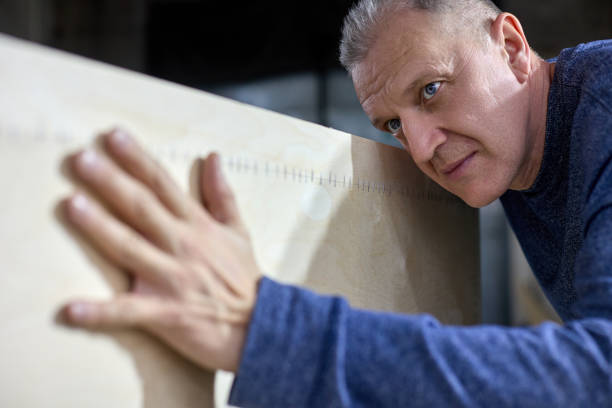 Mature carpenter checks the quality of the plywood frame. Inspection and quality control of the work performed or the quality of wood. Gray haired master receptionist at the furniture production.