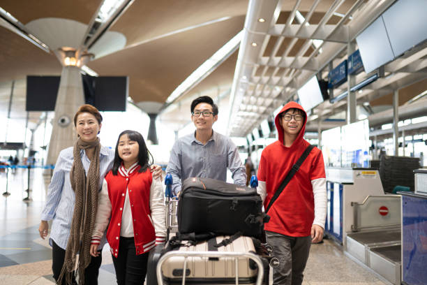 Asian Chinese family walking with their kids and luggage through airport terminal. stock photo