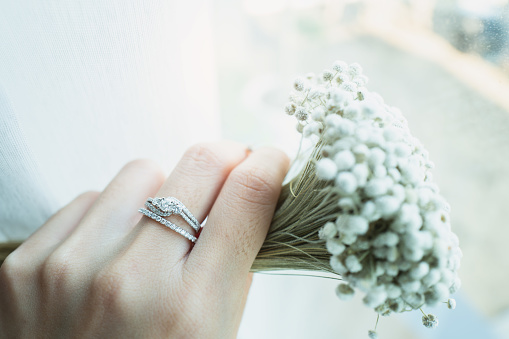 Close up of an elegant diamond ring on woman finger while holding the flower with sunlight background. love and wedding concept. Soft and selective focus.
