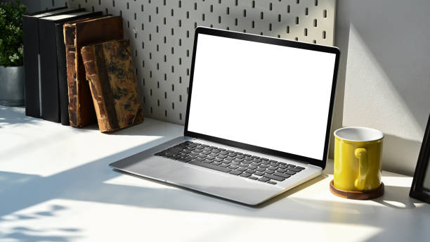 istock Mockup laptop computer with empty display, coffee cup and books on white table. Home office workplace concept. 1385314532