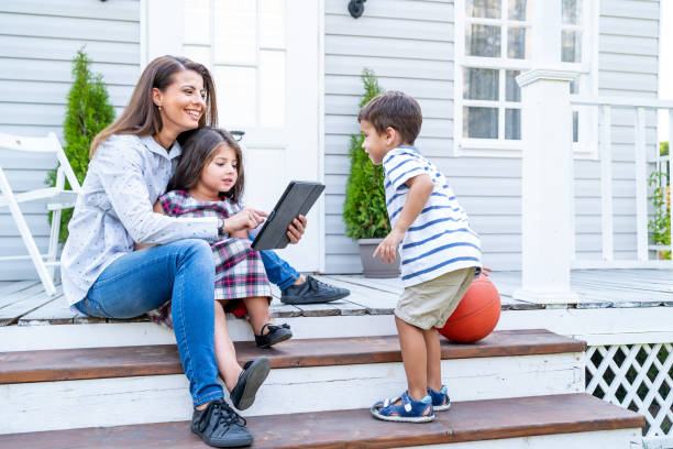 어머니의 샷, 그녀의 두 아이와 함께 현관에 서서 그녀의 작은 딸과 함께 디지털 태블릿을보고 - front stoop outdoors house contemporary 뉴스 사진 이미지