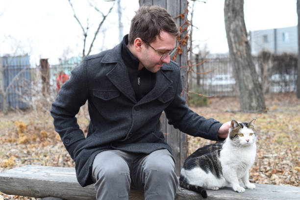 istock Young man sitting on a bench and petting a cat 1385318310