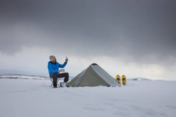 Man snowshoeing and spending vacation in the nature. Using smartphone to talk online with friends.