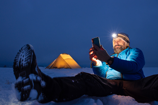 Man snowshoeing and spending vacation in the nature. Using smartphone to talk online with friends.