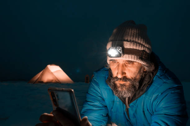 istock Mature tourist using phone at night while tent camping in winter mountain alone in nature. 1385323549
