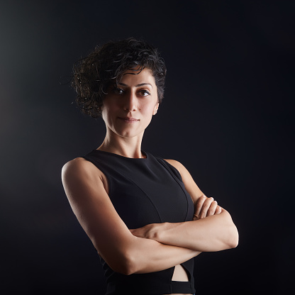 Pretty young woman with curly hair  in casual clothing looking at the camera against a dark studio background with copy space