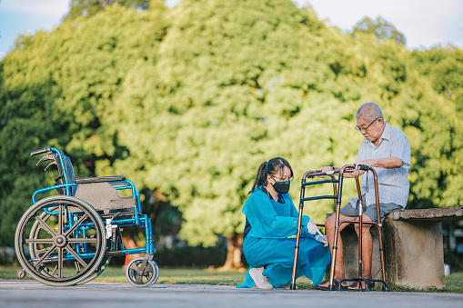 asian chinese female physical therapist guiding senior man stretching exercising his legs at public park
