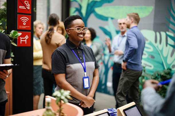 Conference staff members stand by the registration table waiting for the attendees to check-in Black woman, working as a staff during conference event, standing by the registration table education registration event stock pictures, royalty-free photos & images