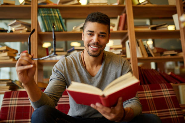istock Smiling African American student enjoying book reading in library 1385337889