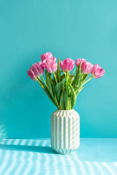 istock Beautiful pink tulips stands in a modern vase on a blue background 1385362569