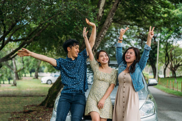 istock Three friends on a road trip taking a break, leaning on the car waving to camera 1385374219