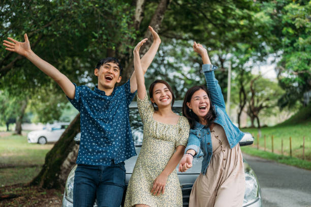 istock Three friends on a road trip taking a break, leaning on the car waving to camera 1385374230