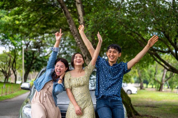 istock Three friends on a road trip taking a break, leaning on the car waving to camera 1385376947