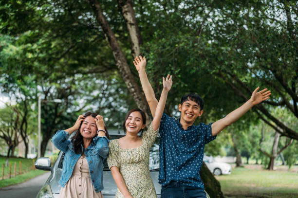 istock Three friends on a road trip taking a break, leaning on the car waving to camera 1385376948